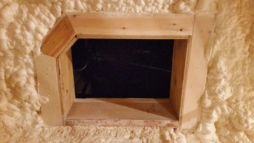 A wooden hole surrounded by spray foam insulation