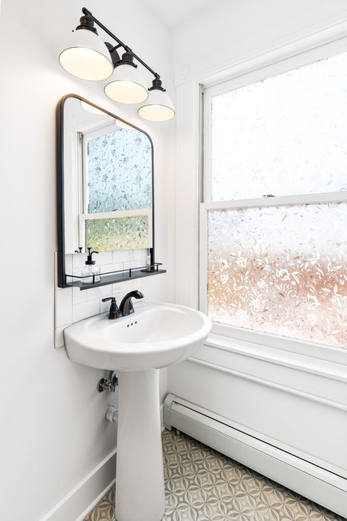 Image of a bathroom with a big window, mounted lights, and tall mirror